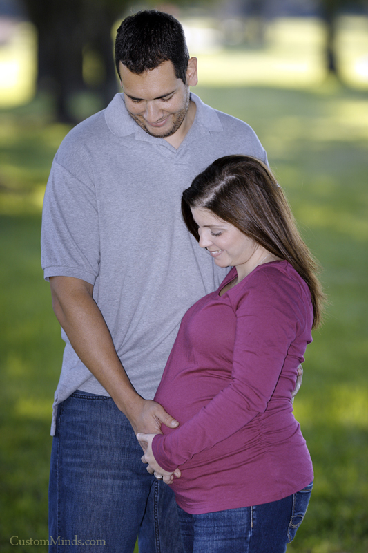 husband and wife in the park holding belly