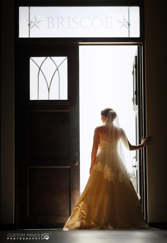 Light floods past a bride in the doorway at Briscoe Manor in Richmond Texas
